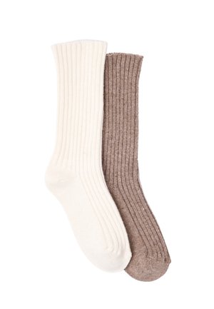 Dos calcetines de canalé de media caña, uno de color crema y otro marrón, aparecen superpuestos sobre un fondo blanco.