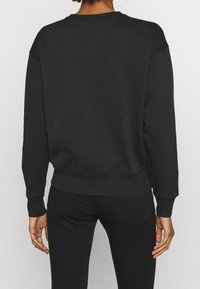 Zwarte trui met een ronde hals en geribbelde manchetten, met een losse pasvorm en een gladde textuur, gecombineerd met strakke zwarte broek.