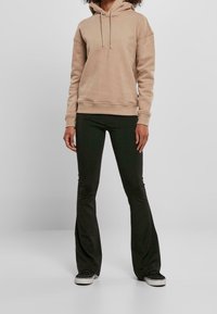 Sudadera con capucha beige con bolsillo frontal, combinada con pantalones acampanados negros. La sudadera tiene cordones y puños acanalados; textura de tela suave.