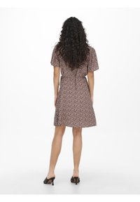 Kurzärmliges Kleid mit floralem Muster in Violett- und Beigetönen, tailliert und mit A-Linien-Schnitt, kombiniert mit schwarzen High Heels.