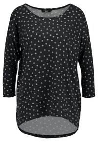Schwarzes Langarmoberteil mit weißem, kreisförmigem Punktmuster. Rundhalsausschnitt und asymmetrischer Saum. Weiche Stofftextur. Lässige Passform.