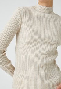 Beige ribbed turtleneck neulepaita, jossa on pitkät hihnat, ohuilla pystysuorilla raidoilla ja tiukalla siluetilla. Pehmeä, teksturoitu kangas.