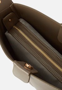 Interno della borsa marrone con una tasca imbottita con zip. Foderato con un motivo a spina di pesce nero e grigio. Dettagli della zip e della ferramenta in oro.