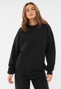 Svart sweatshirt med hög krage och sänkta axlar. Tillverkad i mjukt tyg, med ribbade ärmslut och en avslappnad passform.