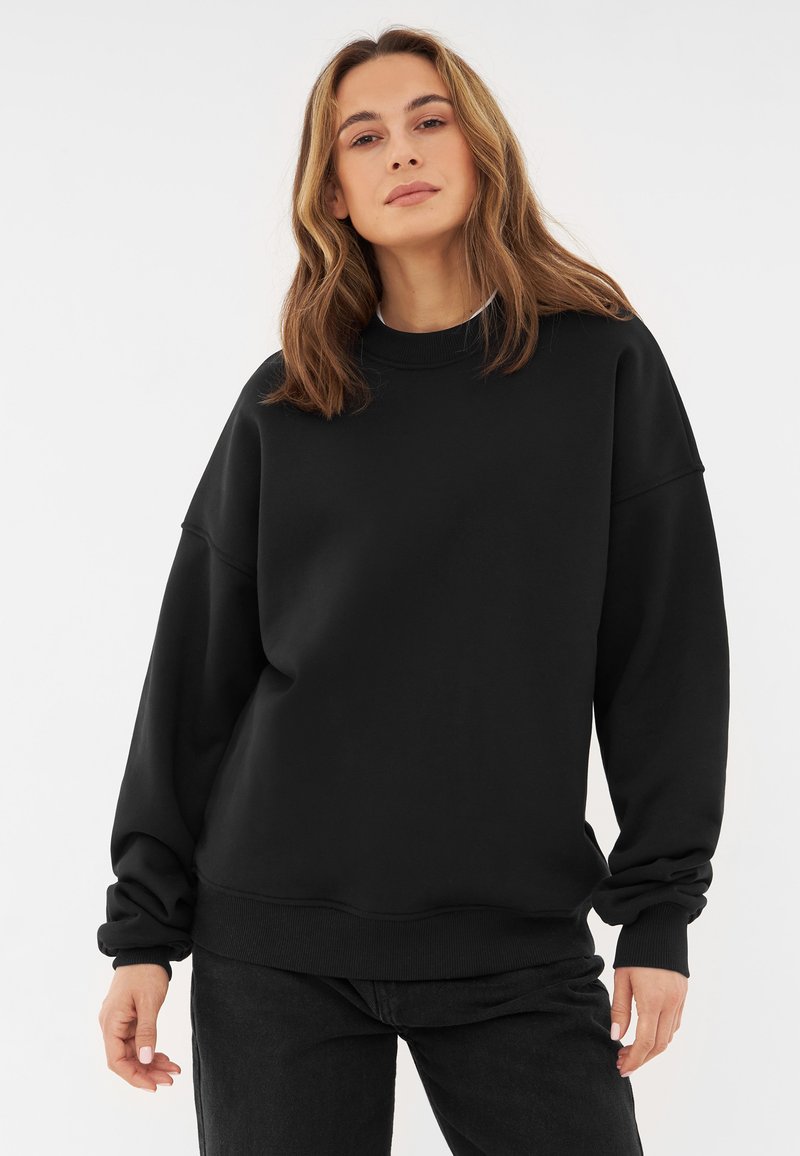 Svart sweatshirt med hög krage och sänkta axlar. Tillverkad i mjukt tyg, med ribbade ärmslut och en avslappnad passform.