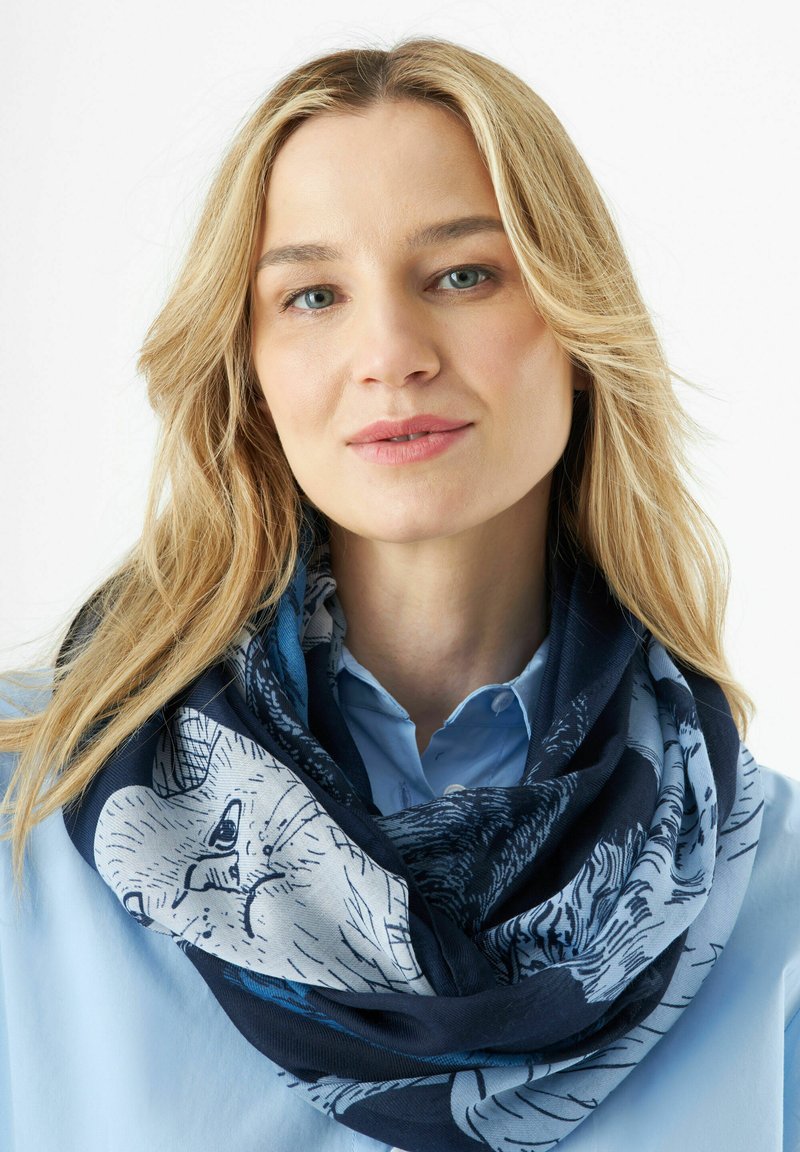 Écharpe bleue marine et claire à motifs avec des illustrations d'animaux, en tissu doux, enroulée lâchement autour du cou, présentant des textures riches.