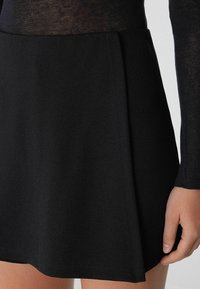 Gonna svasata nera realizzata in tessuto morbido; presenta un design svasato con una texture liscia e dettagli di orlo curati. Vista ravvicinata con mano visibile.