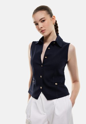 Gilet sans manches bleu marine avec col, comportant des boutons dorés et des poches latérales. Le tissu semble lisse et structuré, renforçant l'aspect soigné.