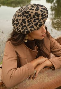 Lapsējuma druku berete mīksta filca materiālā, ar apaļu formu un smalku augšējo daļu. Valkāta ar brūnu zamša jaku. Eleganti aksesuāri.