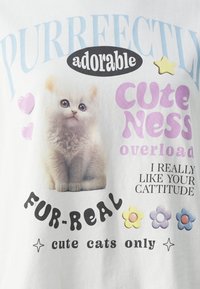 T-shirt en coton blanc mettant en avant un graphique d'un chaton duveteux, du texte coloré, des cœurs et des fleurs dans des teintes pastel.