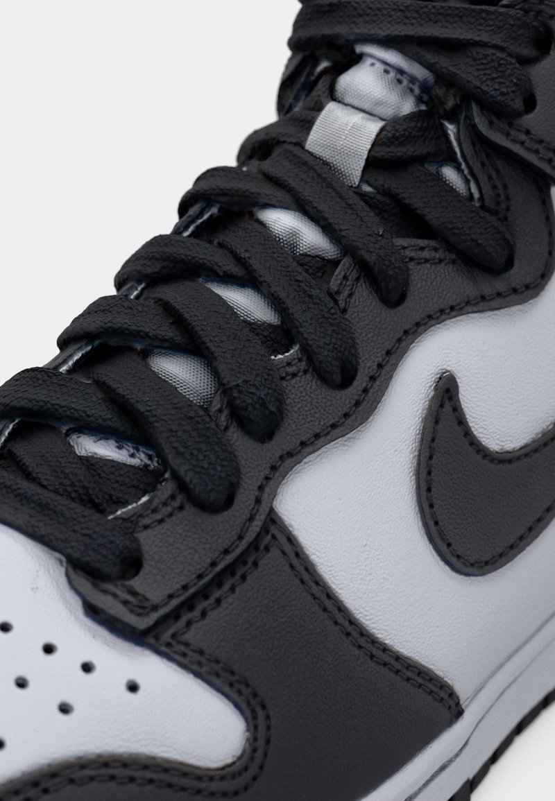 Baskets noir et blanc avec une tige en cuir lisse, des perforations rondes sur l'avant du pied et des lacets plats. Logo Nike notable en noir.