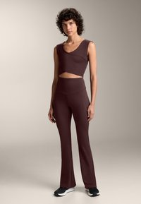 Setul de îmbrăcăminte sport de culoare burgundy include un top scurt cu detaliu decupat și pantaloni evazați cu talie înaltă, realizat dintr-un material neted și elastic.
