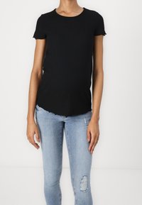 Top negro de manga corta con relieve, de cuello redondo y bordes en forma de onda, combinado con jeans skinny desgastados en azul claro.