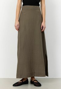 Gonna verde oliva lunga fino alla caviglia in tessuto leggero, con uno spacco laterale per facilitare i movimenti. Abbinata a scarpe piatte nere intrecciate.