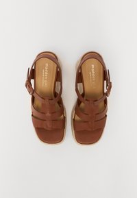 Sandali marroni con cinturini e suola in espadrille, dotati di fibbia regolabile, caratterizzati da un design a piattaforma piatta e una texture in pelle liscia.