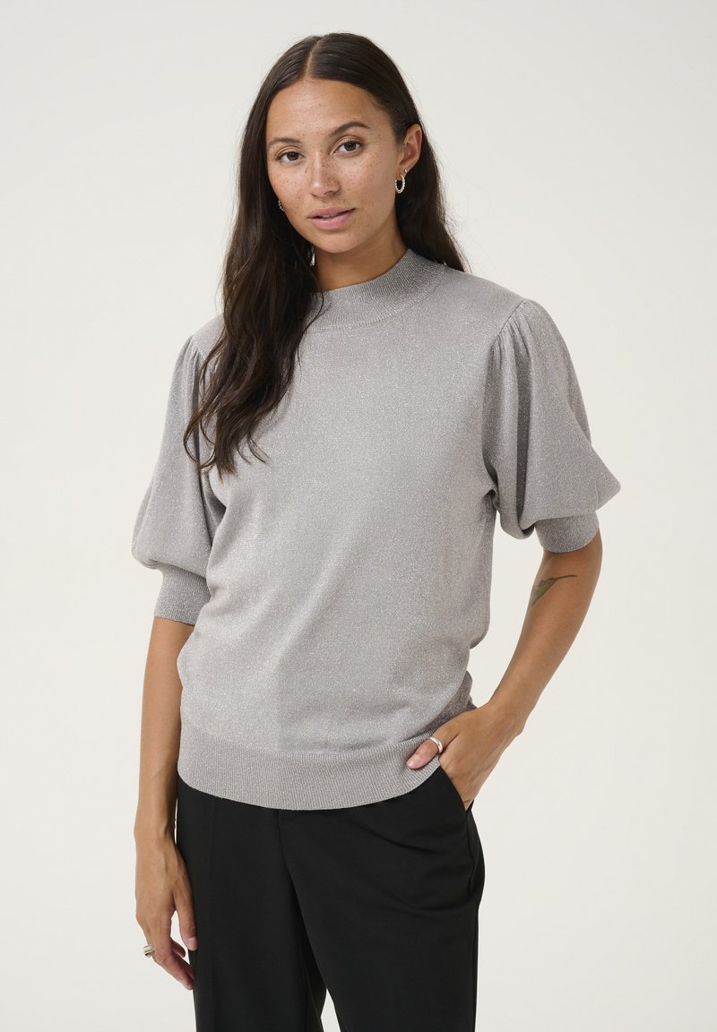 Pull en tricot gris clair avec des manches bouffantes courtes, un col côtelé haut et une finition texturée. Associé à un pantalon noir ample.