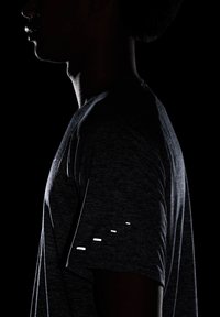 Camiseta deportiva negra con textura jaspeada, que presenta cortes reflectantes en la manga. El diseño enfatiza una silueta ajustada.