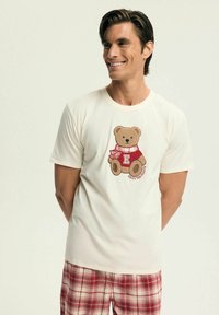 Biały bawełniany t-shirt z haftowanym misiem w czerwonym swetrze i kraciastej szaliku, poniżej napis „Enjoy the Season”.