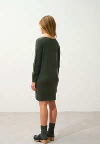 Abito a maglia verde scuro con texture a coste, maniche lunghe e lunghezza appena sopra il ginocchio. Abbinato a zoccoli neri e calze verdi coordinate.