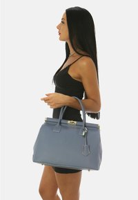 Bolso de mano de imitación cuero azul con forma estructurada, asas superiores y detalles en hardware dorado. Presenta un acabado texturizado y una etiqueta desmontable.