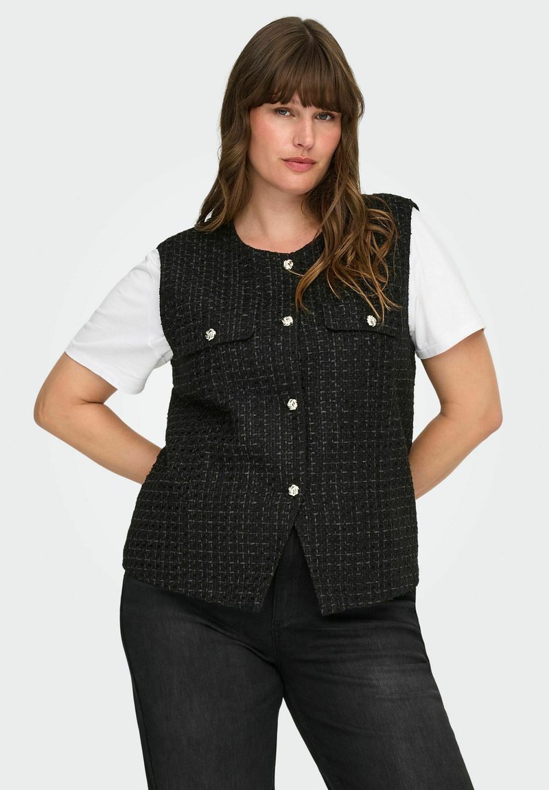 Črn teliran telovnik z okroglim izrezom, sprednjo zapenjanjem na gumbe in dvema našitkoma. Nošen čez belo majico s kratkimi rokavi in kombiniran s črnimi hlačami.