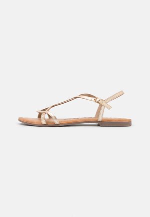 Sandalias planas con tiras metálicas doradas, diseño de punta abierta y plantilla marrón. Incluyen una correa ajustable en el tobillo para un ajuste seguro.
