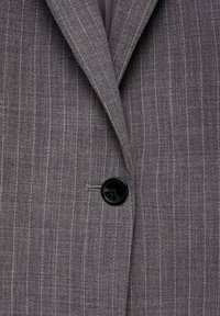 Grey pinstriped blazer made of fabric with a slightly textured finish. Features a single black button and sharp lapels.