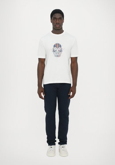 Camiseta de algodón blanca con un gráfico colorido de una calavera en el frente, combinada con pantalones azul marino y zapatillas blancas. Cuello redondo simple.