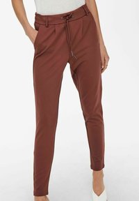 Brązowe, dopasowane spodnie z elastycznym pasem, bocznymi kieszeniami i zwężanymi nogawkami. Wykonane z gładkiego, elastycznego materiału.