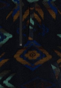 Pullover in pile con mezza zip, con uno sfondo scuro e motivi geometrici in tonalità blu, verde e marrone con una texture morbida.