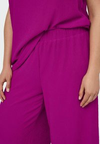 Vêtement texturé magenta comprenant un haut à coupe ample et un pantalon à taille élastique, mettant en avant un tissu doux avec de délicates plis verticaux.