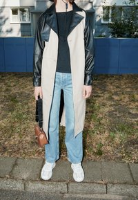 Beżowo-czarny skórzany płaszcz z dużym kołnierzem, zestawiony z jasnoniebieskimi dżinsami. Akcesorium to mała brązowa torba z czarnym paskiem. Białe trampki.