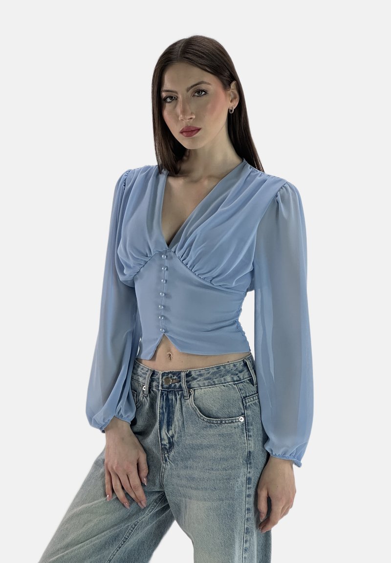 Hellblaue Bluse mit langen, gepufften Ärmeln, V-Ausschnitt, gerafftem Vorderteil, verziert mit kleinen Knöpfen, kombiniert mit hoch taillierten Jeans.
