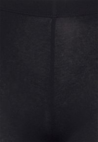 Leggings noirs en tissu extensible et lisse. Dotés d'un design uni avec un léger éclat et sans motifs ni accents visibles.