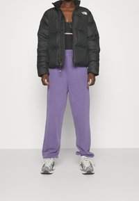 Czarna puchowa kurtka z wysokim kołnierzem, fioletowe spodnie dresowe i jasnoszare buty sportowe z czarnymi i białymi akcentami. Codzienny strój sportowy.