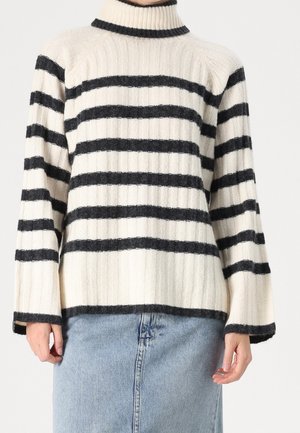 Pull à col roulé côtelé couleur crème avec des rayures noires horizontales, porté avec une jupe en jean bleu clair.