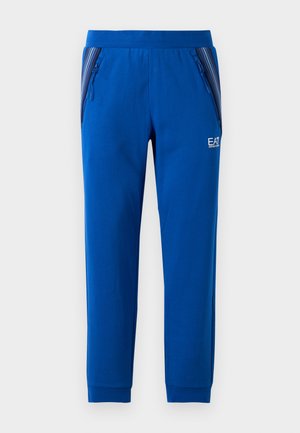 Pantaloni blu in morbido tessuto con design a gamba dritta. Presentano due cerniere laterali e un logo sul davanti. Accenti a righe sulle tasche.