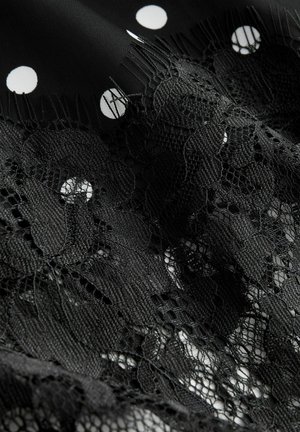 Black fabric with white polka dots features intricate black lace detailing, showcasing varied textures and patterns in a layered design.