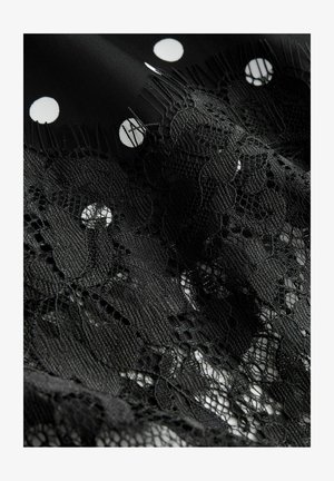 Mustast kangast, millel on valged täpilised täpid, esineb keerukaid musta pitsi detaile, mis näitavad kihilisi mustreid ja erinevaid tekstuure.