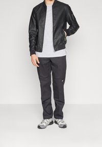 Schwarze Lederbomberjacke, graues T-Shirt, dunkle Hose mit Taschen und graue Sportschuhe mit gemusterten Schnürsenkeln. Schlichter, moderner Look.