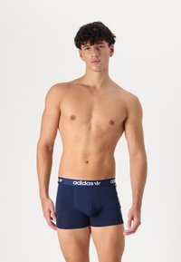 Marineblaue Baumwollunterhose mit einem weißen elastischen Bund, der das "adidas"-Logo und drei Streifen an den Seiten aufweist. Glatte Textur, figurbetontes Design.