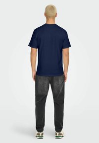 Marineblå bomulds t-shirt med rund hals og korte ærmer, iført med grå denim bukser og sko med grønne accenter.