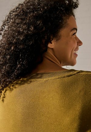 Pull texturé couleur moutarde avec un col côtelé, présentant une coupe décontractée et des éclats subtils dans des couleurs variées.
