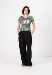 Kamuflasje t-skjorte med "GAP" logo i hvitt; parret med løse svarte bukser. Antrekket har en avslappet passform og mykt stoff.