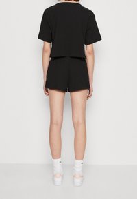 Person wearing black ribbed short-sleeve top and matching shorts, white socks, and white sneakers, standing against a plain background.