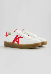 Vita sneakers med röda accenter och en stor "A"-logotyp. Har en slät läderövre och en gumminätsula för bra grepp.