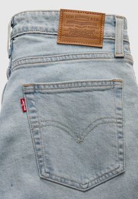 Πίσω τσέπη σε φωτεινό γαλάζιο τζιν με κόκκινη ετικέτα Levi's και κάτω από τη ζώνη, καφέ δερμάτινη ετικέτα Levi Strauss & Co.