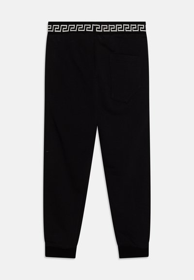 Pantalones de chándal negros con una banda geométrica blanca en la cintura, con un único bolsillo trasero y puños acanalados. Textura de tela suave.