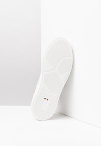 Biała podeszwa sneakerów z teksturowanym wzorem, zaokrąglonym kształtem i wytłoczonym logo marki. Zawiera beżowy akcent i jest wykonana z trwałego materiału gumowego.