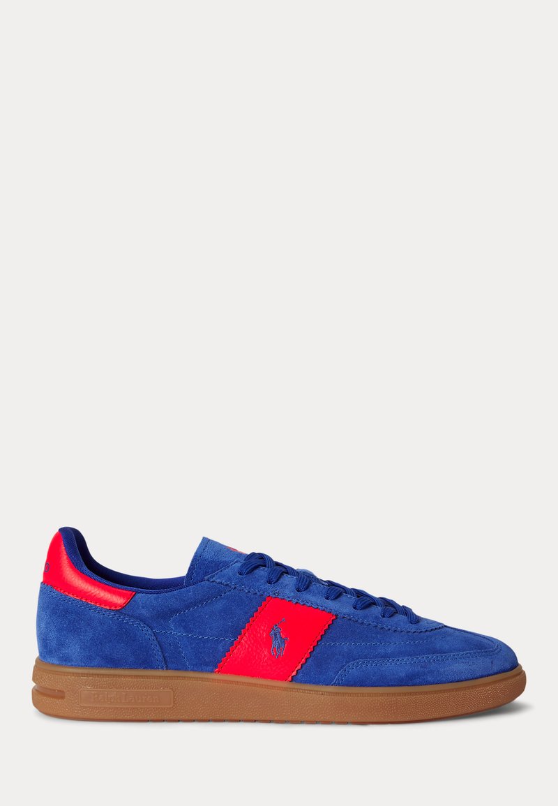 Baskets en daim bleu avec des accents en cuir rouge, des lacets bleus et une semelle en caoutchouc marron, avec un logo rouge sur le côté.
